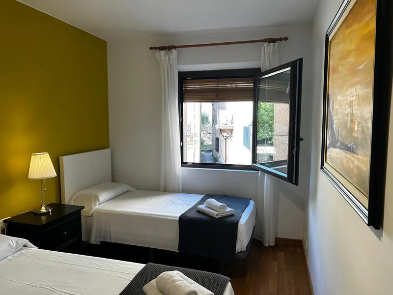 Yellow bedroom with three beds and a window onto the village