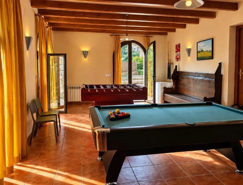 Sala de jocs amb billar, futbolí i porta d’arc oberta a l’exterior