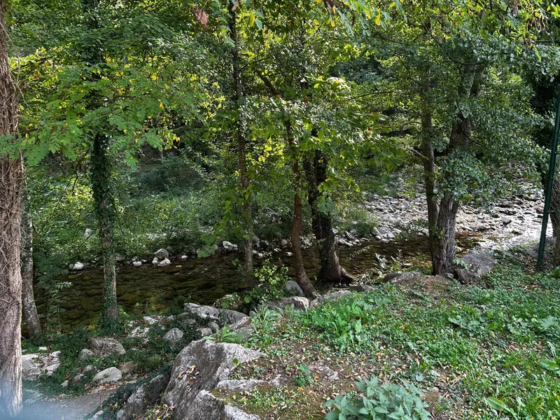 El riu Muga entre arbres i roques, al costat de la casa